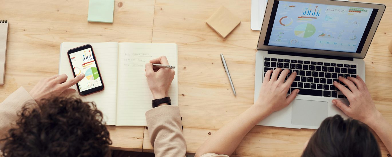 Two marketing professionals analyzing SEO data and business growth metrics on a laptop and smartphone at a wooden desk