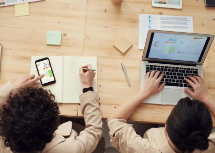 Two marketing professionals analyzing SEO data and business growth metrics on a laptop and smartphone at a wooden desk