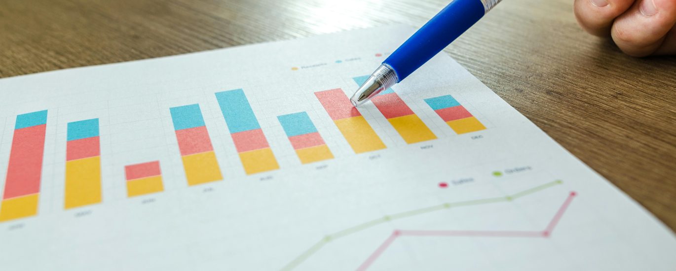Hand pointing at colorful SEO analytics and growth charts on paper, representing search performance and digital strategy planning.