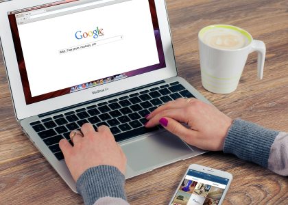 Person using Google search on a laptop with smartphone and coffee on desk, representing local SEO and Google My Business optimization.