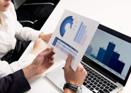Business professionals analyzing SEO performance metrics on a laptop with printed data charts in a strategy meeting.