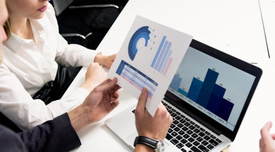 Business professionals analyzing SEO performance metrics on a laptop with printed data charts in a strategy meeting.