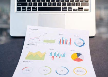 Close-up of a laptop with printed SEO charts and graphs on a dark desk surface, representing website performance and digital marketing analytics.